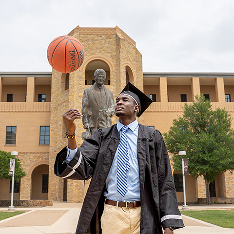 Student in Cap and Gown with Basketball in Front of Madla Statue
